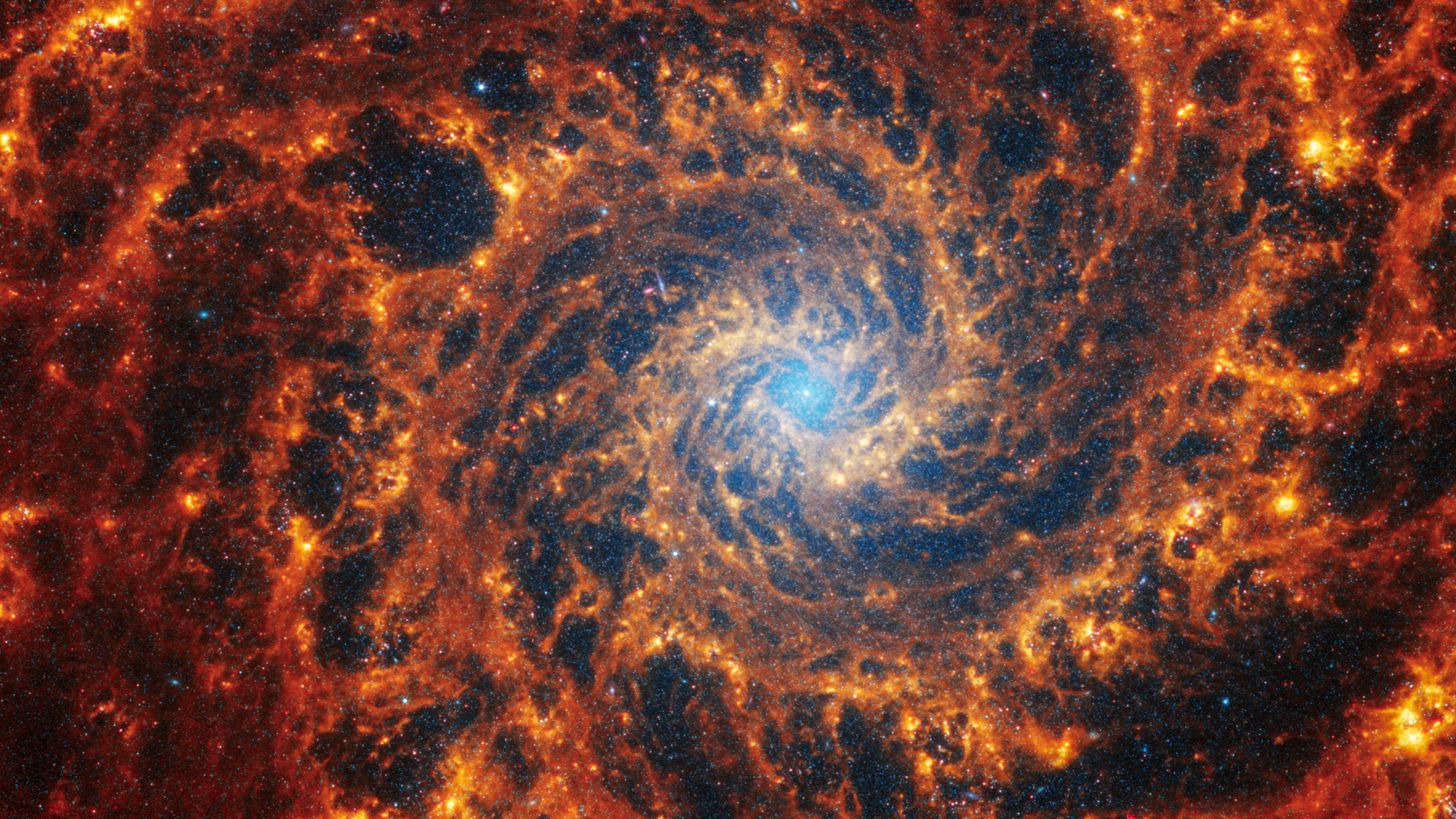 A dramatic spiral galaxy with orange and red arms and a light blue center